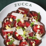 Beef carpaccio garnished with cheese, greens, and a creamy sauce on a Zucca plate.