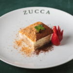 Elegant tiramisu dessert garnished with a strawberry and mint on a white plate.