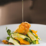 A gourmet dish with fried food and fresh vegetables drizzled with sauce.