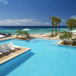 A luxurious pool overlooking the ocean with palm trees and lounge chairs.