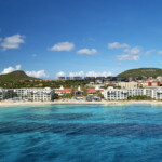 Scenic coastal town with clear blue waters and white buildings under a bright sky.