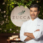 Confident chef posing in front of Zucca restaurant sign.