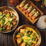 Two bowls of vibrant curry with grilled chicken and cilantro, plus a wooden board with stuffed bread slices.