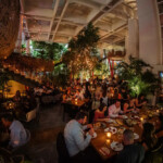 Cozy restaurant filled with diners surrounded by lush plants and warm lights.