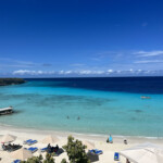 Sunny beach with turquoise water and clear blue sky.