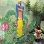 Colorful bird sculpture and mural in a garden corner.