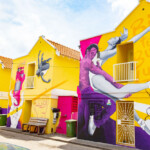 Colorful street art of dancers on vibrant yellow and pink buildings.