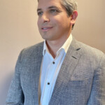 Man in grey blazer and white shirt smiling softly.