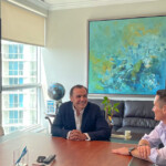Two men in conversation at a conference table in a bright, modern office.