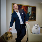 Man in suit posing with two dogs in a living room.