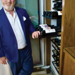 Man in a blue suit standing next to a wine rack.