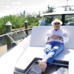 Man relaxing barefoot on a yacht in casual attire and hat.
