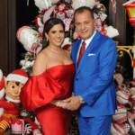 A couple dressed elegantly, posing by a festive Christmas tree.
