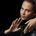 Serious woman with focused expression, hands raised defensively against a black background.