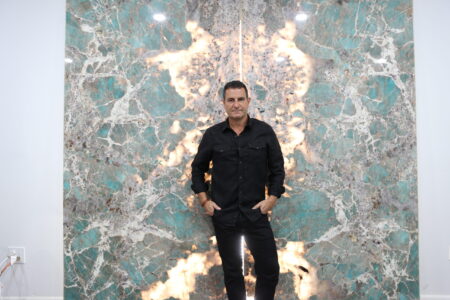 Man in black shirt posing against a textured marble wall.