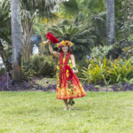 A dancer in a vibrant tropical costume performs outdoors.