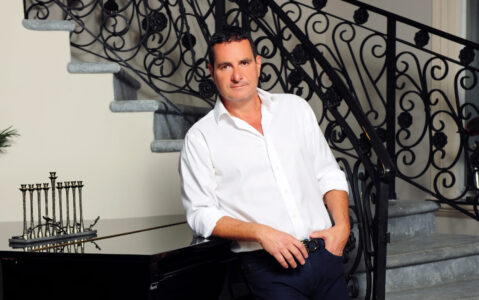 Man in white shirt posing by staircase with ornate railing.
