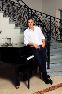 Man in white shirt posing by staircase with ornate railing.