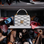Elegant white handbag with gold accents displayed among rolled fabrics.
