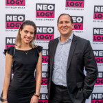 Two professionals posing at a Neology event with branded backdrop.