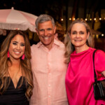 Three people smiling at a nighttime outdoor event with string lights.