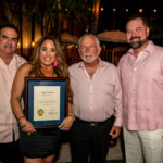 Four people posing with an award plaque in an evening setting.