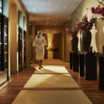 Woman walking in a warmly lit, elegant hallway with floral decorations.