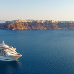 Luxury cruise ship sailing near a scenic volcanic island at sunset.
