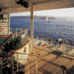 Ocean view from a wooden deck with people and a sailboat in the distance.