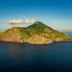 A lush green island surrounded by calm blue waters under a clear sky.