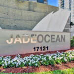 Sign for Jade Ocean condominium with flowers and building in background.