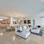Spacious modern living room with white sectional sofa and dining area.