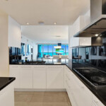 Modern white kitchen with sleek black appliances and large window.