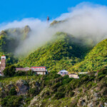 Scenic mountain village with lush greenery and misty clouds.