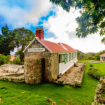 Historic stone church with a red roof and green shutters under a blue sky.