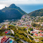 A scenic aerial view of a coastal town with hills and ocean in the background.