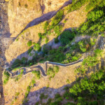 A winding stone wall traverses a rugged mountainous landscape with greenery.