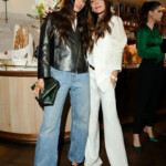 Isabela Grutman, Victoria Beckham Two women posing stylishly in casual chic outfits at an indoor event.