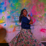 Woman posing joyfully in front of a colorful graffiti wall.