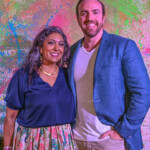 A man and woman smiling together against a colorful wall.