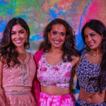Three smiling women in colorful, festive attire against a vibrant backdrop.