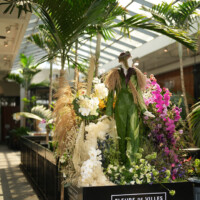 A lush indoor garden display with orchids and tropical plants under a glass roof.