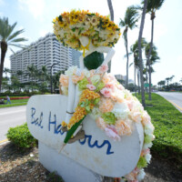 A floral sculpture of a perfume bottle with sunflowers on top outdoors.