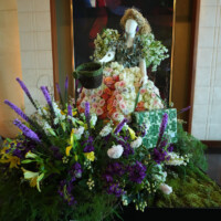 Floral arrangement with a doll centerpiece in traditional attire surrounded by vibrant flowers.