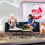 Three women engaged in a lively talk show set of "La Mesa Caliente."