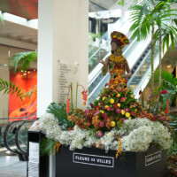 Floral sculpture of a woman made from colorful flowers in a public space.
