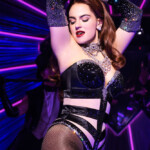 A woman in glamorous black outfit dancing in a vibrant club.