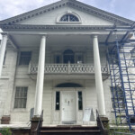 Old two-story house with white pillars and scaffolding for renovation.