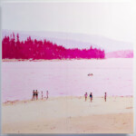 People enjoying a beach with forested hills in the background.