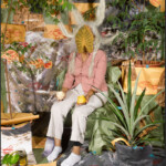 Person in a pink jacket surrounded by plants in a colorful, rustic setting.